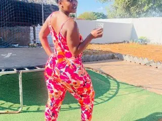 BUSTYBOOTYY poses outdoors in a colorful floral jumpsuit while holding a drink near a trampoline.