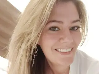 Smiling blonde woman in a white outfit enjoying a bright, cheerful moment indoors.