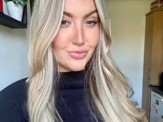 BabydollPaige poses with her long blonde hair framing her face, wearing a black turtleneck top.