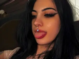 Young woman with long black hair and winged eyeliner sticking her tongue out in a moody close-up portrait.