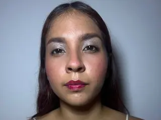 Barbbyhott looks directly at the camera with long dark hair and light eye makeup, showing her face and shoulders against a plain background.