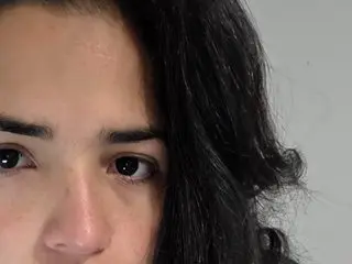 Beatrixxx25 looks directly at the camera with her long, dark wavy hair framing her face in a close-up shot.