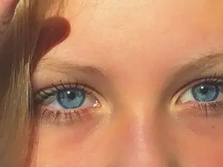 Close-up portrait of a young woman with bright blue eyes and long eyelashes in warm natural sunlight.