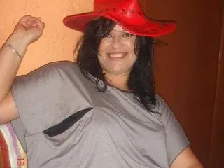 BeautifulDream smiles while wearing a red cowboy hat and a grey t-shirt, posing with one arm raised against a warm orange background.
