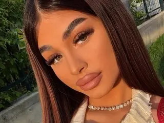 BellaNoirre poses outdoors in the sunlight with long dark hair and glamorous makeup.