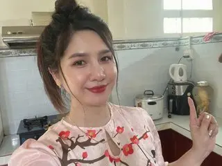 BellaTran looks at the camera with a smile, wearing a pink patterned top with her dark hair tied up in a bun.