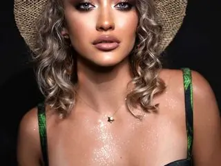 Glamorous woman in a straw hat and green patterned bikini with shimmering skin against a dark background.