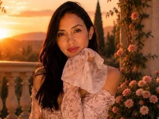 BelladonnaLips poses outdoors in a pink floral top during a golden sunset.