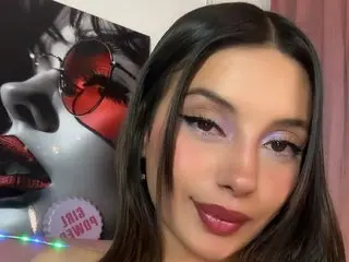 Bellanovacs looks directly at the camera with a soft smile, showing her long dark hair and light purple eyeshadow.