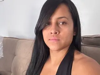 Bellaobsesion poses with long black hair, looking directly at the camera in a close-up shot against a neutral background.