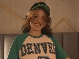 Bennywilson smiles wearing a green and white Denver t-shirt with her curly brown hair down.