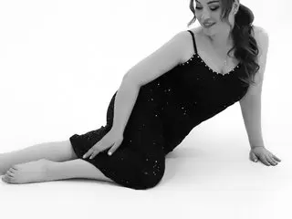 Bettyb777 poses sitting on a white floor, wearing a black spaghetti strap dress with her long hair down.