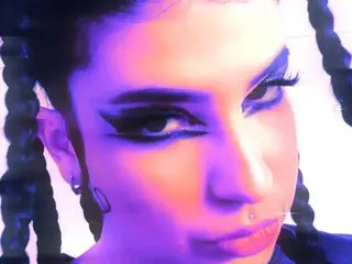 BeyondSteel poses with a direct gaze, showing her dark hair and heavy eyeliner against a bright background.