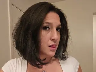 Bi_sexualmilf looks at the camera with her tongue out, showing her dark hair and white top in a close-up shot.