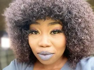BigBurstyBelly poses with a close-up view of her face, showing her dark curly hair and grey lipstick.