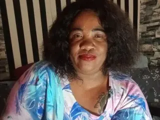 BigHotMatureXXXX has dark curly hair and red lipstick, wearing a blue and white patterned top while looking directly at the camera.