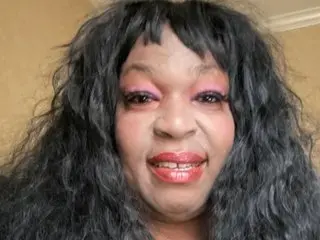 BigVickie smiling at the camera with long, wavy black hair and pink eyeshadow.