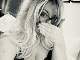 BlondeBridgetx wearing glasses and looking at the camera while covering her face with her hand.