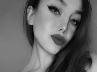 BlueEyedBrooke poses with a head tilt, showing her long dark hair and facial features in a black and white close-up.