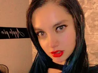 BlueeEclipsee poses close-up with long dark hair and bright red lipstick, looking directly at the camera.