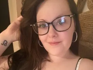 BobbieGalore poses with her hand in her long dark hair, wearing black-rimmed glasses and large hoop earrings.