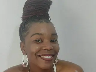 BoityLips smiles close-up, showing her dark hair styled in a high bun and wearing large white hoop earrings against a plain background.