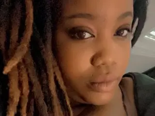 BombshellChasity poses close-up, showing her face and long dark dreadlocks against a dark background.