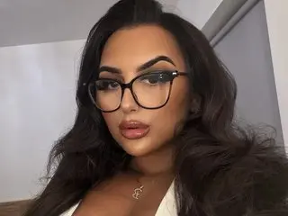 Bonniemaexx poses with long wavy dark hair and black glasses, looking directly at the camera in a close-up shot.