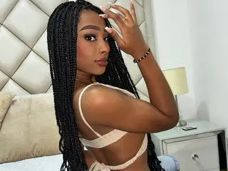 BonnySullivan18 poses with her hands near her face, showing her long dark braids and wearing a white bra or bikini top.