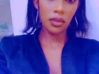 BoomOrBust poses close-up, looking at the camera with dark hair and large hoop earrings, wearing a dark v-neck top.