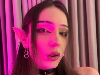 BoyTemptation looks into the camera with long dark hair and pink eye makeup, wearing a black choker against a soft pink background.