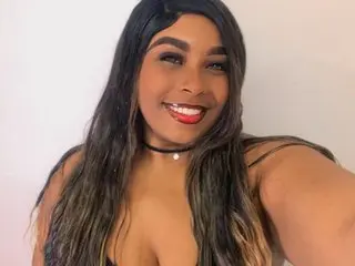 BrainMansonh smiles with red lipstick, wearing a black choker and a black top, with her long dark hair styled down.