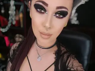 Brattygeorgie poses close-up, showing her face, dark eye makeup, and a black lace choker or neckband.
