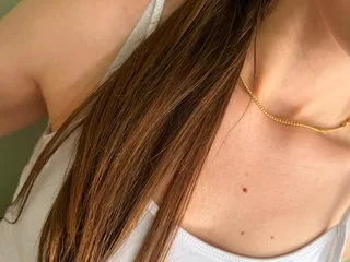 Brianna00 wears a white tank top and a gold necklace while looking toward the camera.