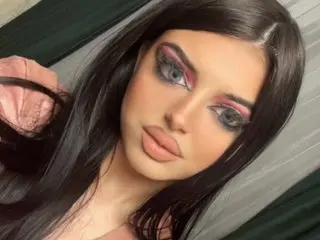 Young woman with long dark hair and glamorous pink eye makeup posing in a soft indoor setting.