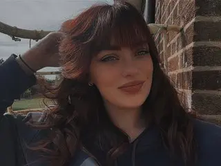 BrunetteBrooklyn poses with her long, wavy dark hair and bangs, looking directly at the camera with a soft smile.