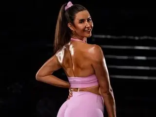 Smiling woman in pink fitness outfit posing with glowing skin in a dark studio setting.