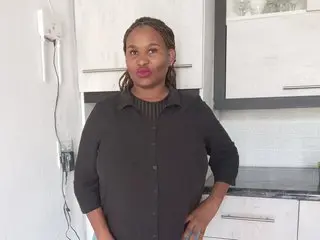 Confident woman in a black button-down shirt standing in a modern white kitchen.
