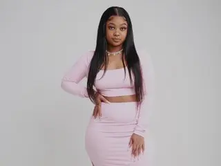 Young woman in a stylish pink two-piece crop top and skirt outfit posing against a neutral studio background.