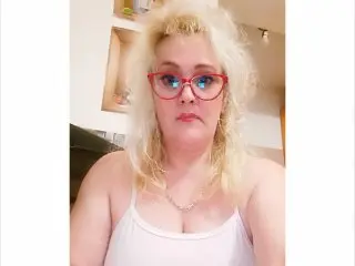 CATALEYIA, a blonde woman, wearing a white tank top, looking directly at the camera with a neutral expression.