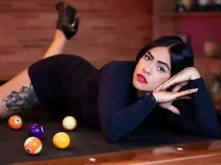 Glamorous woman in a black dress lounging on a pool table with billiard balls in a moody lounge setting.