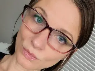 CallMeDaisy looks into the camera with her brown hair down, wearing red-rimmed glasses and a light pink lipstick.