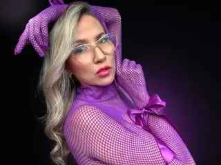 CallieMartin poses in a purple fishnet top and matching gloves, looking directly at the camera with her long blonde hair styled down.