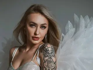 Beautiful blonde woman with arm tattoos wearing a white sequin angel costume with large feathered wings.