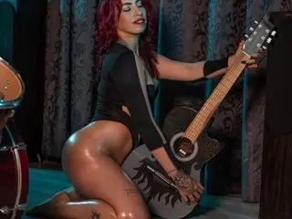Red-haired woman in a black bodysuit playing an acoustic guitar in a moody, dimly lit studio setting.