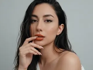 CarlaParkeer poses with her hand near her mouth, showing her long dark hair and bare shoulders against a plain grey background.