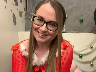 Smiling woman in a red and white festive Christmas outfit sitting in a cozy holiday-themed room.