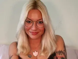 Cat_xx has long blonde hair and wears thin-rimmed glasses, looking directly at the camera with a slight smile.