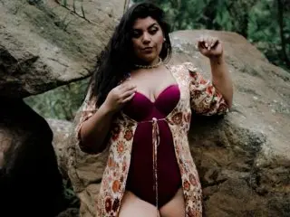 CatalinaSainz_S poses in a patterned red and white robe, showing cleavage and her bare legs against a natural outdoor background.