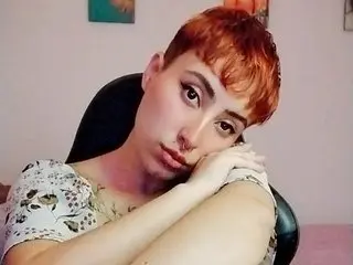Catsito poses with her arms crossed, showing her face, short red hair, and a white floral patterned top.